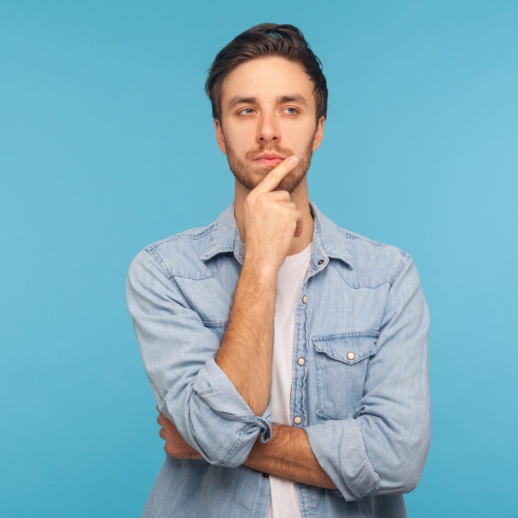 Hmm, let's think! Portrait of pensive handsome man in worker denim shirt touching chin while pondering plan Resources portal - pondering plans, difficult choice, not sure
